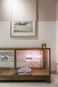 Modern retail storefront with a glass and wood display case containing mugs, a neon sign, and a backpack.
