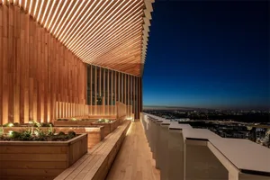 A wooden terrace with planters and a wooden structure at dusk overlooking a cityscape.