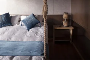 A minimalist bedroom featuring blue and white textiles, a wooden headboard, and a wooden bedside table with a decorative ligh