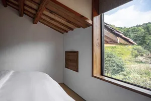 A minimalist bedroom with a white bed and a large window overlooking greenery.