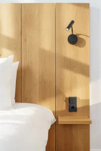 Minimalist bedroom with a bed, white pillows, and a wall-mounted bedside lamp with wooden panels.