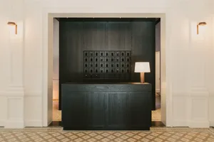 Modern reception desk with dark wooden finish, illuminated by a table lamp and located at the entrance of an elegant lobby.