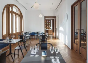 Modern restaurant interior with wooden floors, tables, and chairs, featuring a contemporary design with white walls and large