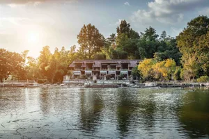 A traditional architectural building situated by a tranquil lake surrounded by lush greenery and trees.