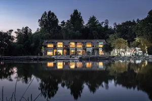 A traditional house with wooden and stone exterior by a calm lake, reflecting the house in its surroundings.
