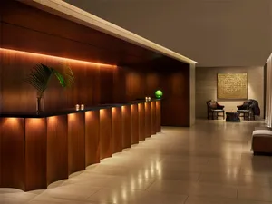 Modern, luxury hotel reception area with wooden finishes, illuminated by warm, ambient lighting, featuring a sleek, minimalis