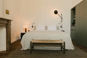 Minimalist bedroom with a bed dressed in white textiles and a woven bench.