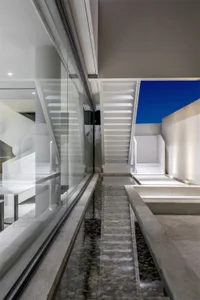 Modern minimalist interior space featuring a concrete pond and stairs, with a glass wall and a blue sky background.