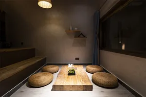 A minimalist living space featuring a wooden table surrounded by rattan cushions, under warm lighting with a modern aesthetic