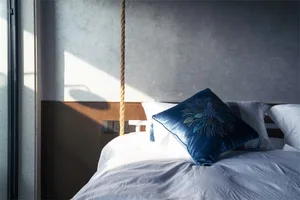 A modern bedroom with white cotton bedding, a blue decorative pillow, and a wooden headboard.