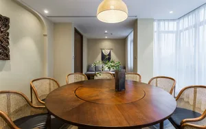 Modern dining room featuring a circular wooden table surrounded by rattan chairs and a potted plant centerpiece.