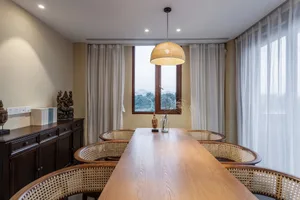 Modern dining room featuring a large wooden table, wicker chairs, and a view through the window.