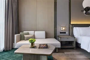 A modern minimalist hotel room featuring a comfortable seating area, a side table with a vase and a book, and a bed.