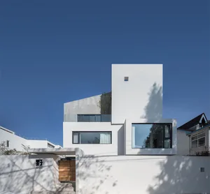 Modern residential exterior with white concrete walls and glass windows.