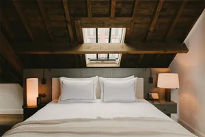 A modern minimalist bedroom with a double bed, white linens, and a skylight in the ceiling.