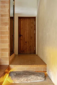 Modern minimalist doorway with stone steps, wooden door, and brick wall.