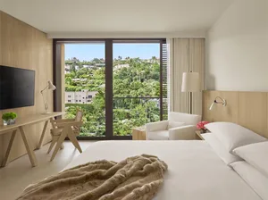 A modern minimalist hotel bedroom featuring wood, glass, and fabric materials.