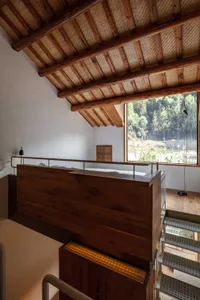 Staircase with wooden railings and floor, featuring a view of greenery through a large window.