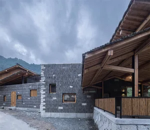 Contemporary residential home exterior featuring stone and wood materials, with a dramatic, cloudy sky in the background.