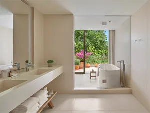 Modern bathroom with white tiled walls, ceramic bathtub, and garden view through glass door.