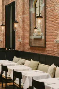 A restaurant interior featuring brick walls, leather cushions, and glass lighting fixtures.