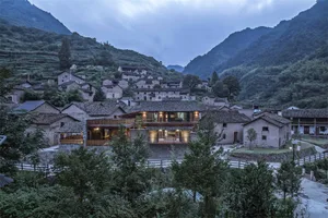 A traditional stone house with a clay-tiled roof nestled among lush green mountains.