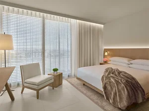 A minimalist bedroom with a bed, nightstands, and a window covered by textured curtains.