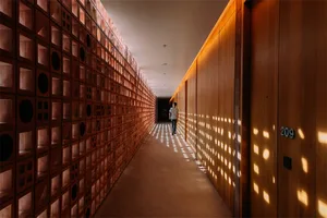 Hallway with minimalist design, illuminated with light fixtures, showing unique wall pattern with light and shadow effects.