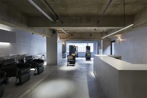 Modern minimalist office space with concrete flooring, exposed concrete walls, and sleek, black chairs.