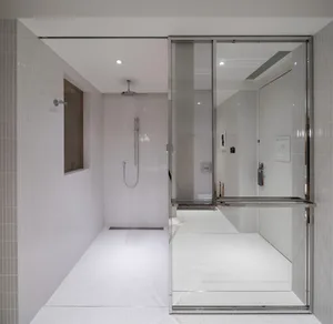 A modern bathroom with white tiled walls and floor, featuring a glass shower enclosure and a minimalist design.