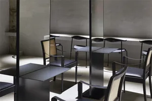 A minimalist dining area featuring modern metal tables with glass tops and black chairs with woven backs.