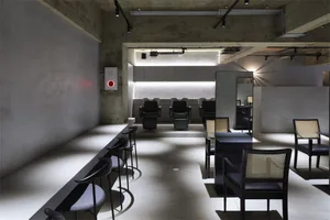 A modern hair salon interior with minimalist design featuring black seating and concrete floors.
