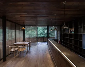 A modern restaurant with wooden interior and floor, featuring a long counter with lighting and a table with chairs in front o