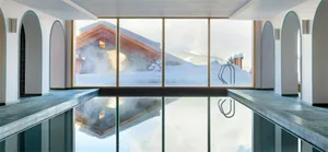 Modern indoor swimming pool with glass walls reflecting a snowy landscape outside.
