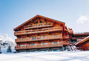 Front view of a multi-story wooden chalet hotel with snowy landscape.