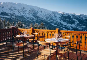 A luxurious restaurant with a wooden deck overlooking a snow-covered mountain range.