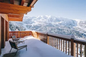 A snow-covered cabin with a wooden balcony overlooking a snow-covered mountain landscape.