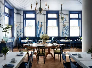 A beautifully designed restaurant interior with blue and white decor, featuring round tables, chairs, and floral arrangements