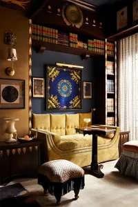 A cozy, eclectic living room with a yellow velvet sofa, bookshelves, and various decorative elements.