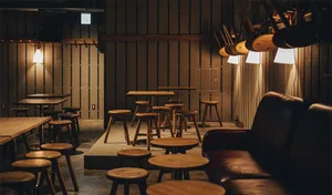 An industrial-style bar area with wooden stools and tables in an open-plan layout.