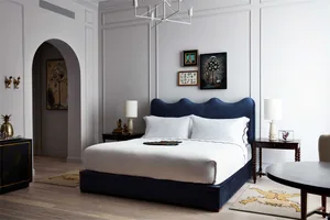 一間極簡臥室，配有白色床鋪、藍色床頭板，以及牆上的裱框藝術作品。