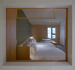 Modern minimalist bedroom with white bedding and wooden furniture, featuring a frame and light fixture.