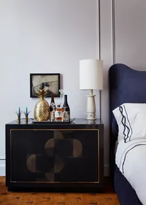 A modern bedroom corner with a black sideboard featuring a brass pineapple ice bucket, a framed artwork, a table lamp, and a 