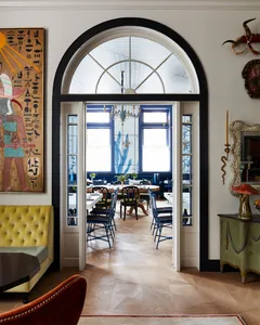 Modern dining room with wooden floors, chairs, and table, featuring a large arched window.