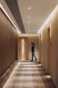 A modern corridor featuring wooden slats and tiled flooring, illuminated by recessed lighting.