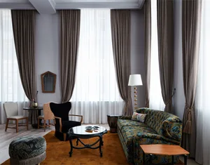 Modern living room with dark wooden floor, plush seating area, and large windows with sheer curtains.