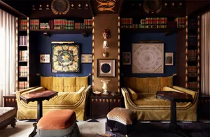 A modern living room with gold upholstery, dark wood accents, and silk artwork on navy walls.