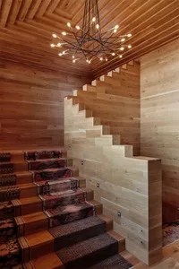 A modern staircase with wood paneling and a unique light fixture in a wooden room.