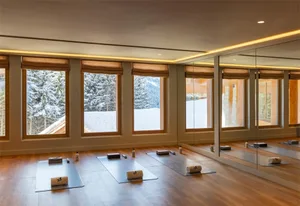 A spacious yoga studio with large windows, wooden floors, and mirrored walls.