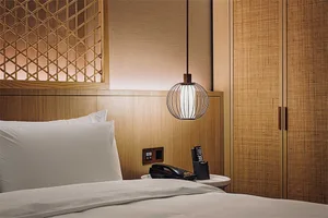 Modern bedroom with brown wood walls, a bed, a light fixture, and a phone on a nightstand.